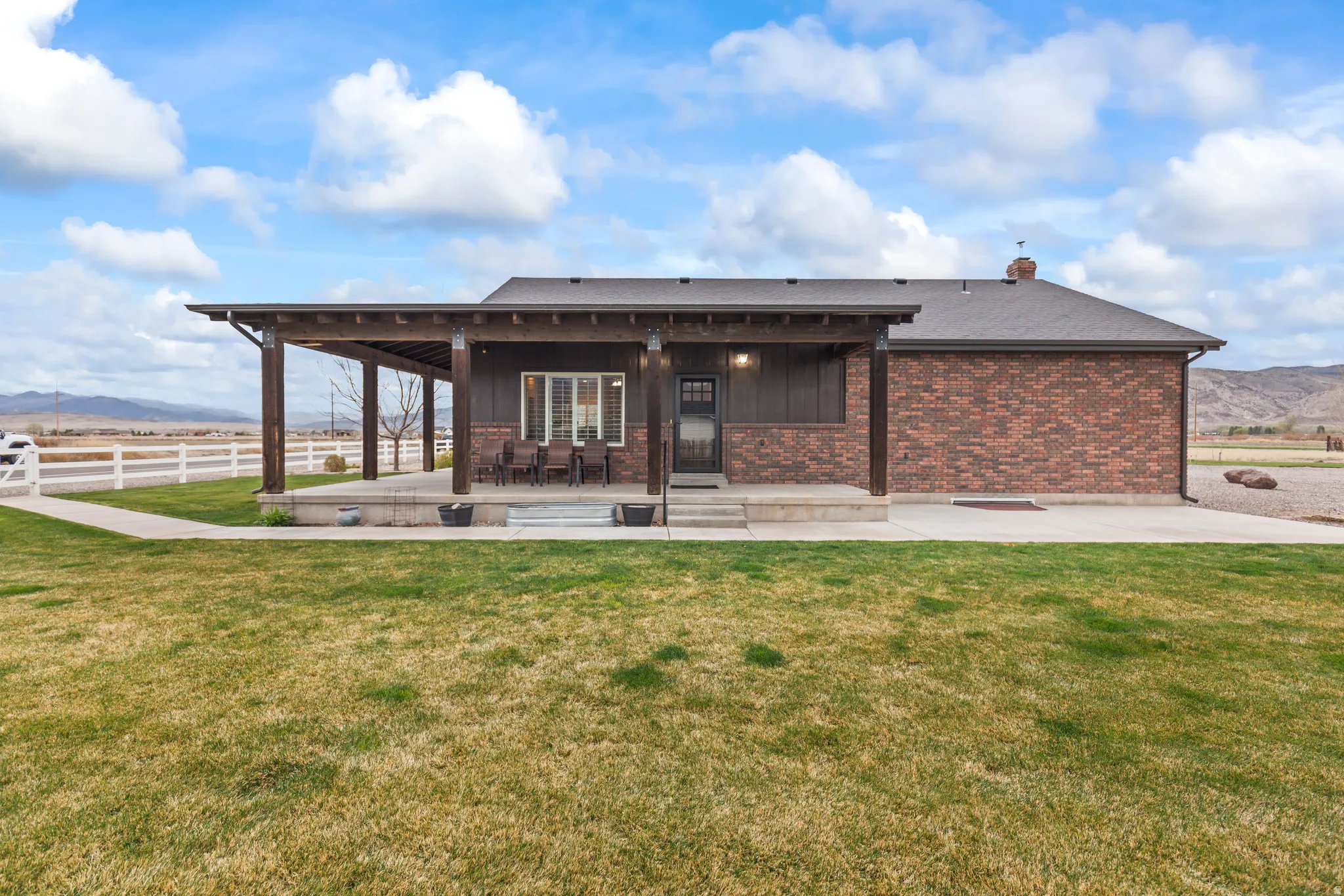 Rear exterior featuring a covered patio with exposed wood beams, brick siding, and a manicured lawn