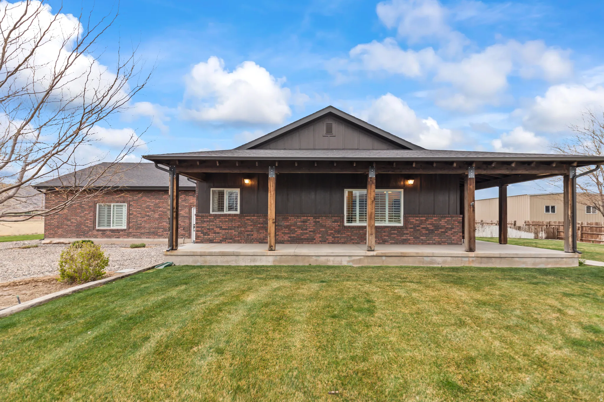 Exterior featuring a covered patio with exposed wood beams and columns, board and batten siding, brick wainscoting, and white-framed windows with plantation shutters