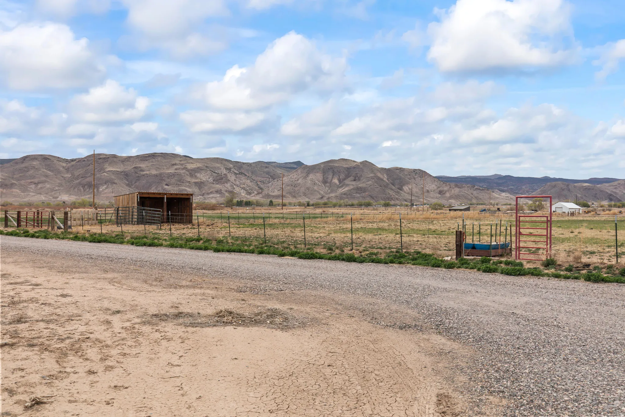 Expansive rural property featuring a gravel road, open fields, and distant mountain ranges