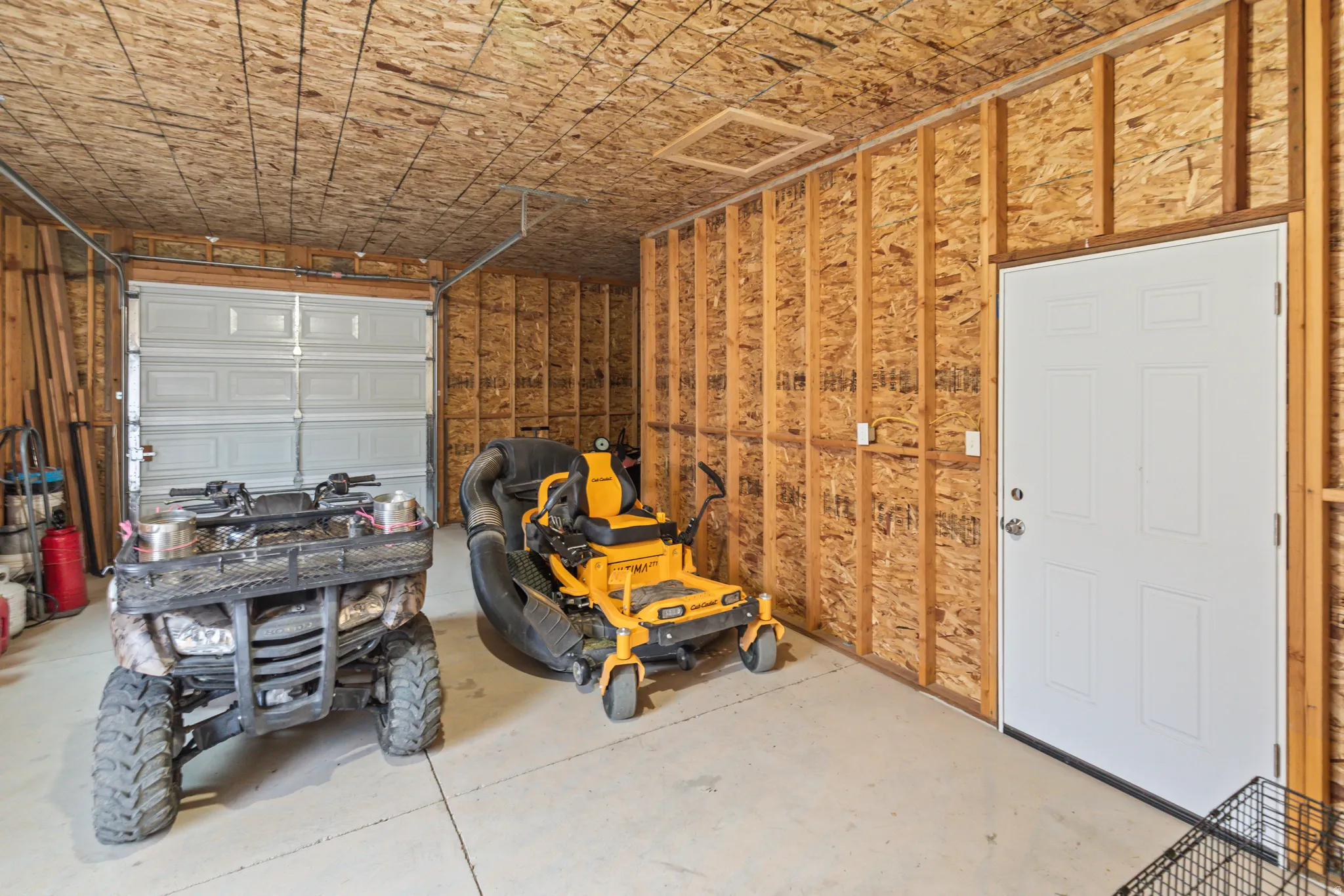 Interior garage featuring a white paneled overhead door, concrete flooring, and exposed wood framing