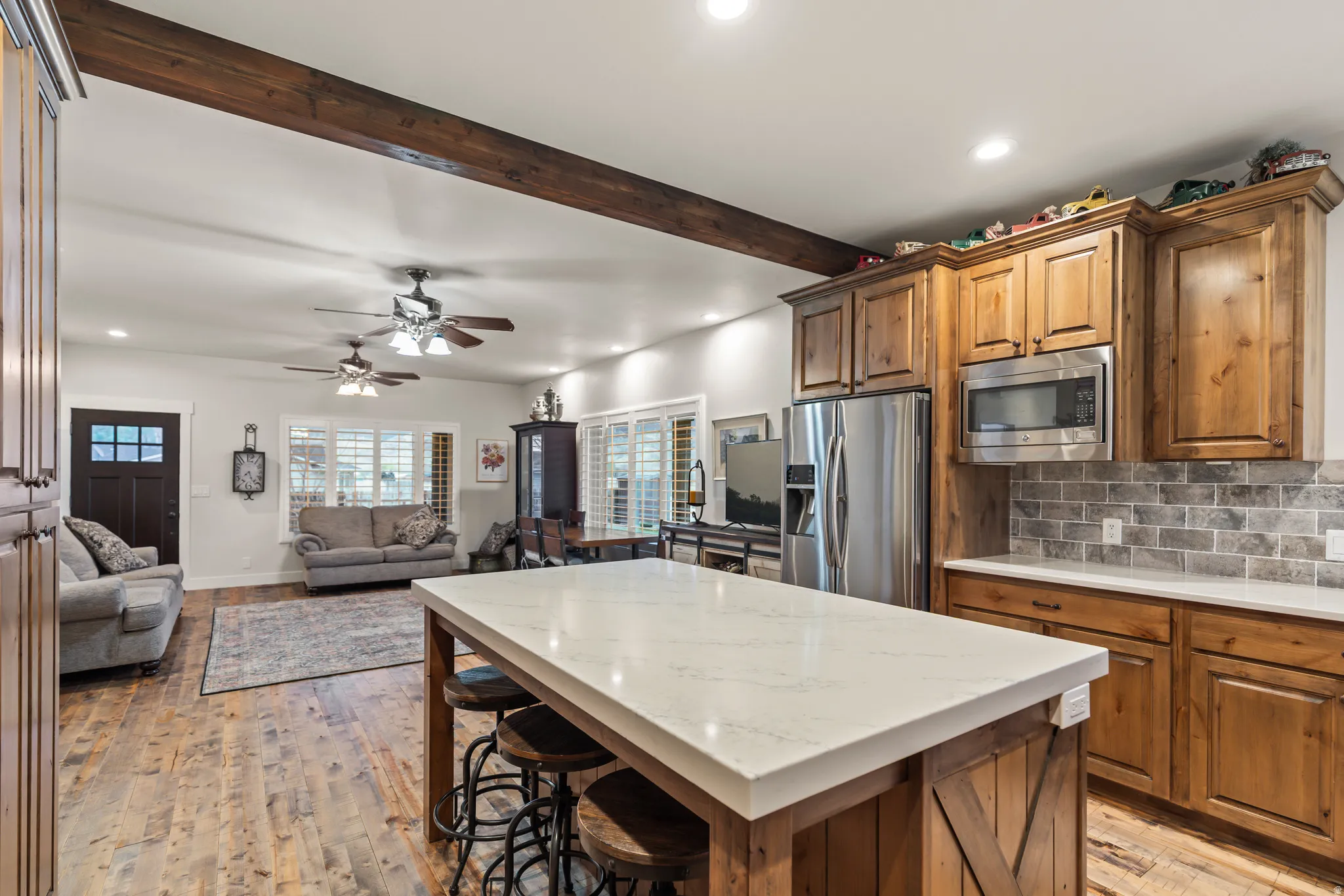 Kitchen island with a white countertop and wood-finish base, stainless steel appliances, wood cabinetry, and a subway tile backsplash