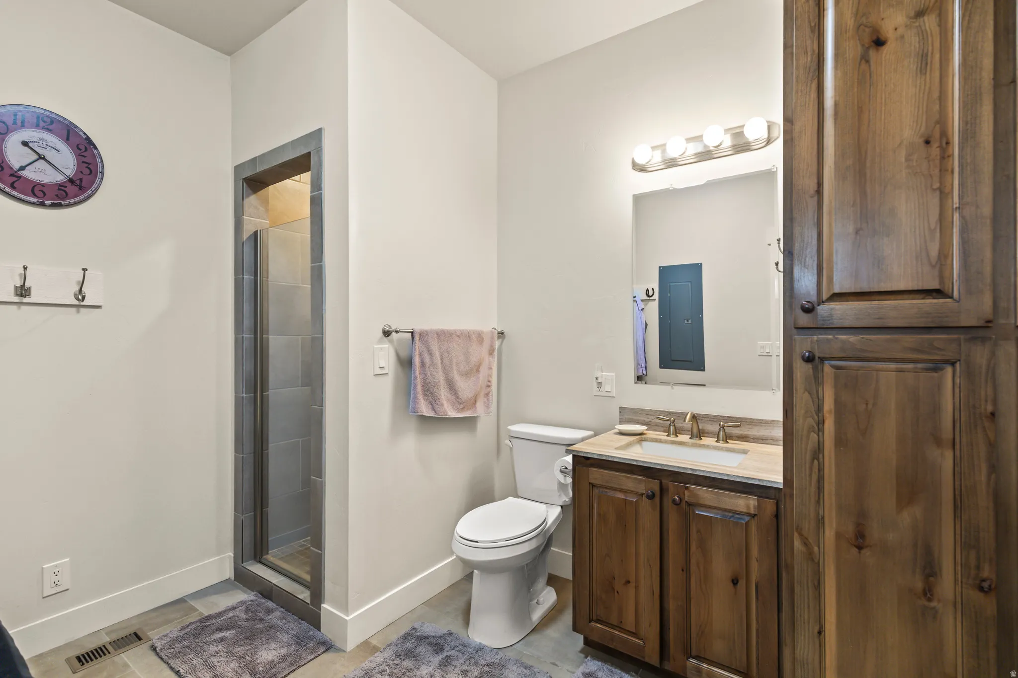 Bathroom featuring a glass-enclosed shower with gray tile surround, wood-finish vanity with an undermount sink and light-toned countertop, and a tall wood-finish storage cabinet