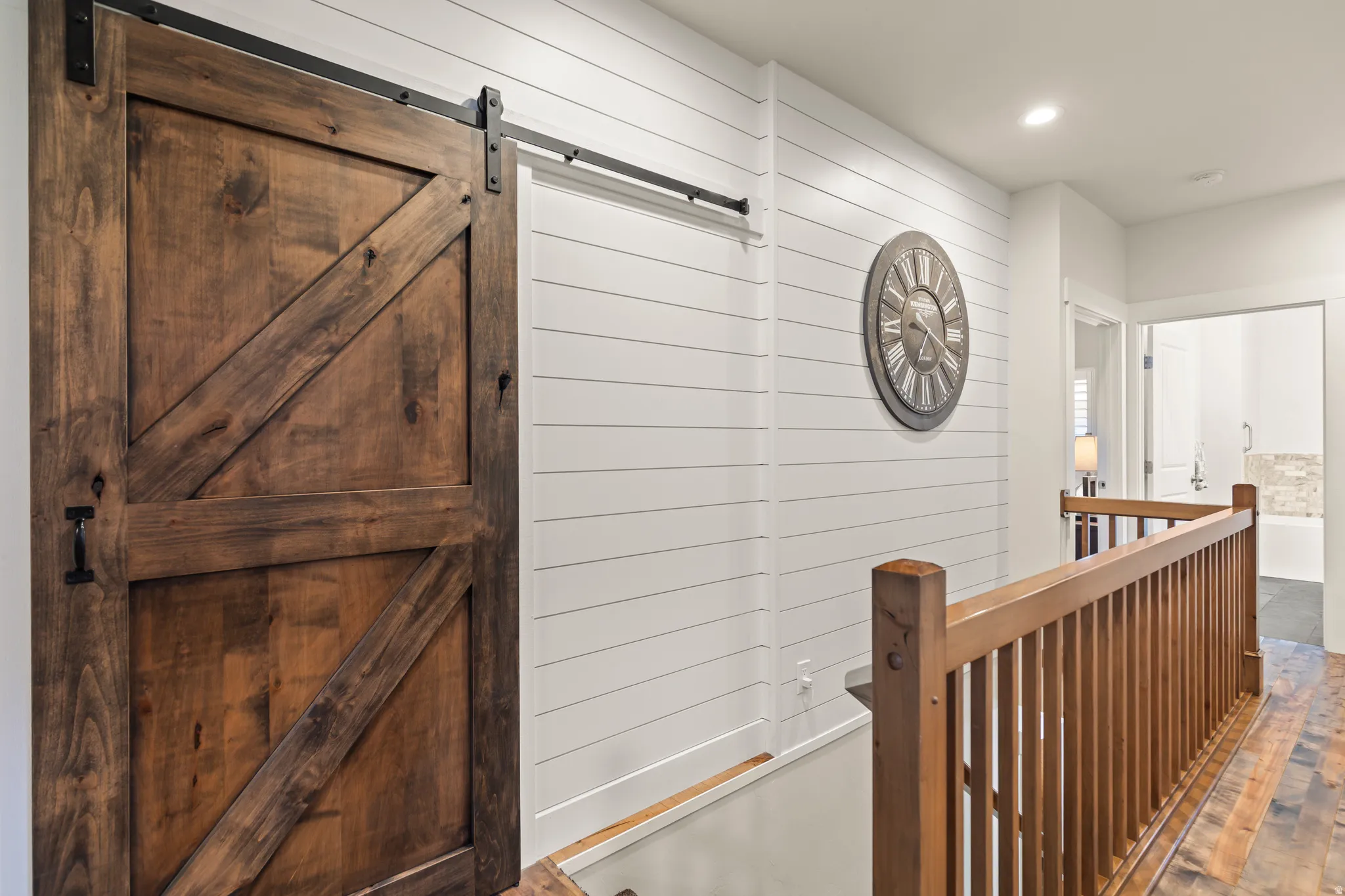 Wood-finish barn door with black hardware, shiplap wall paneling, recessed lighting, and natural wood railing