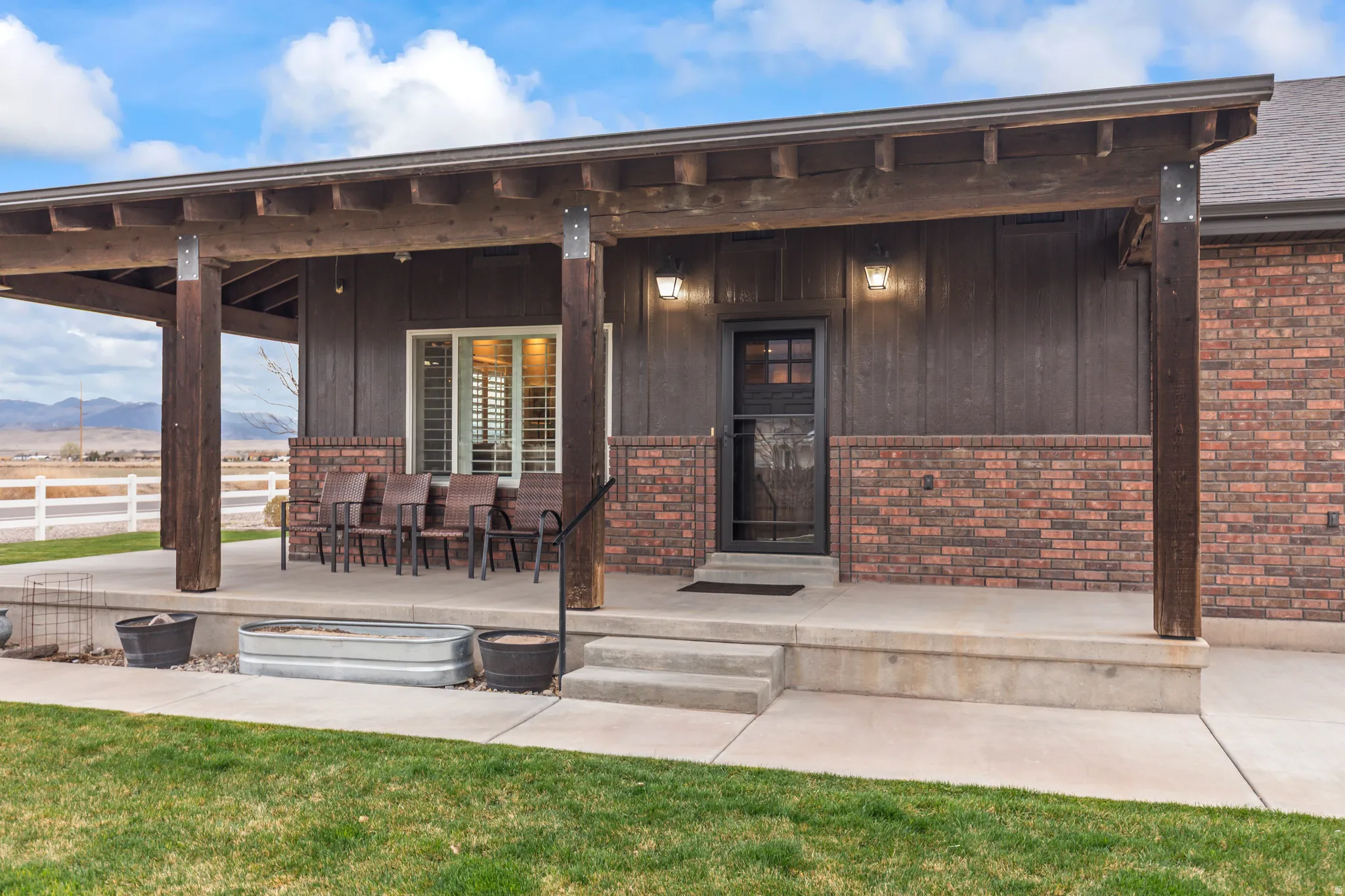 Covered porch featuring a concrete patio, brick wainscoting, wood siding, and robust wood support beams