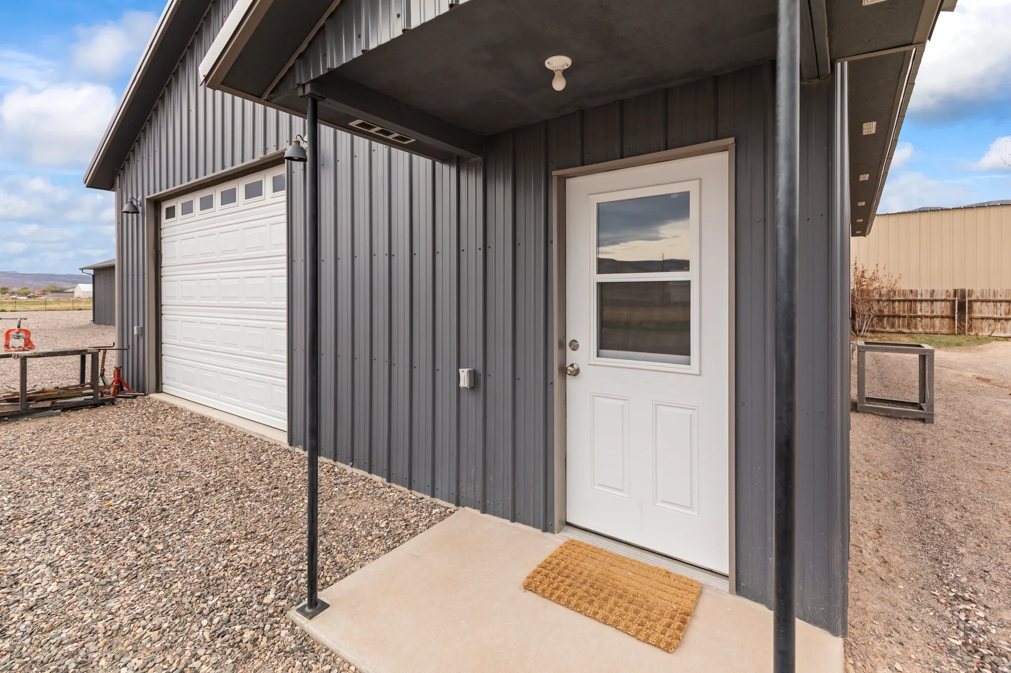 Corrugated metal siding exterior featuring a white paneled entry door with window, a concrete stoop, and a large white garage door with upper window panels