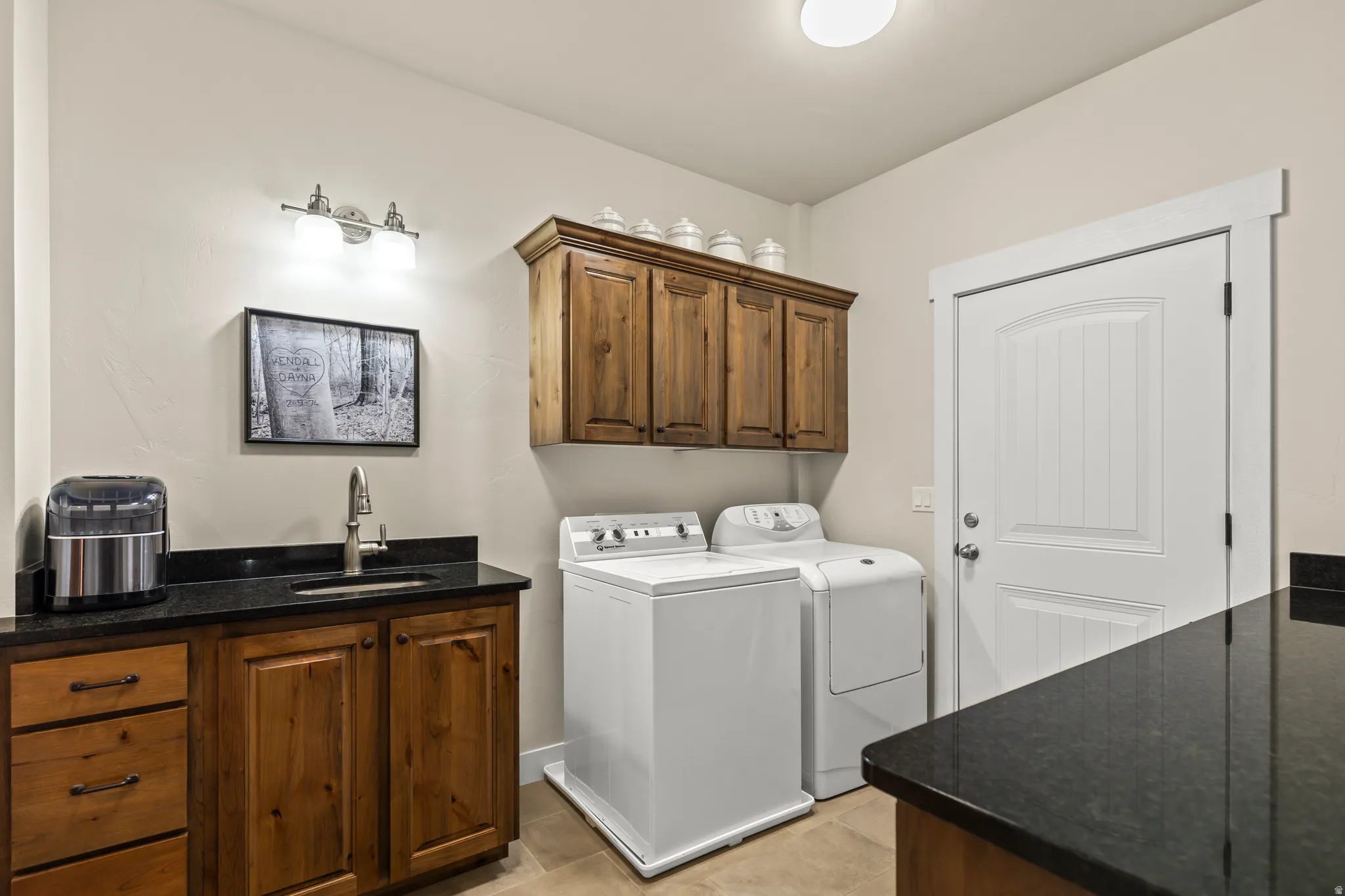 Dedicated laundry area featuring a utility sink with a brushed nickel faucet, dark stone countertops, and wood-finish cabinetry