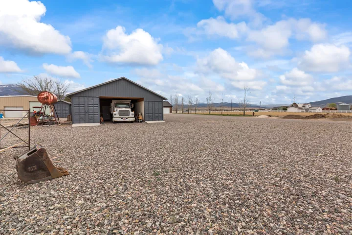 Spacious gravel lot with a large gray metal-sided utility building featuring multiple bay doors and an open bay
