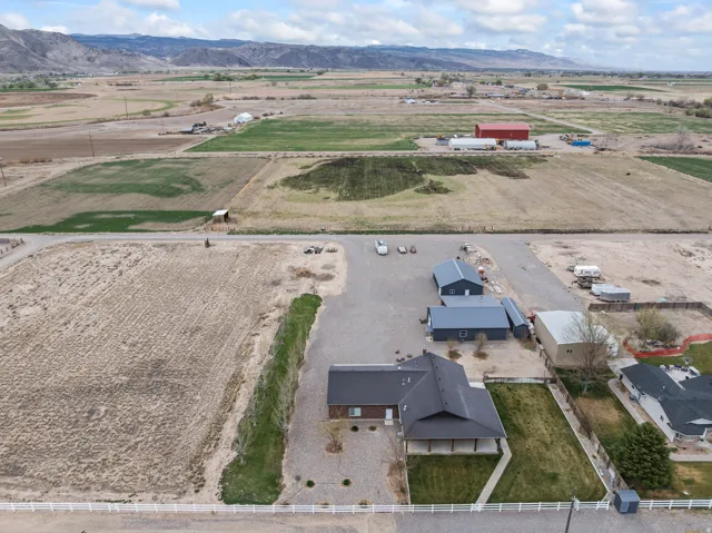 Aerial perspective showcasing the property with a dark-roofed residence, extensive gravel parking, and a manicured lawn area