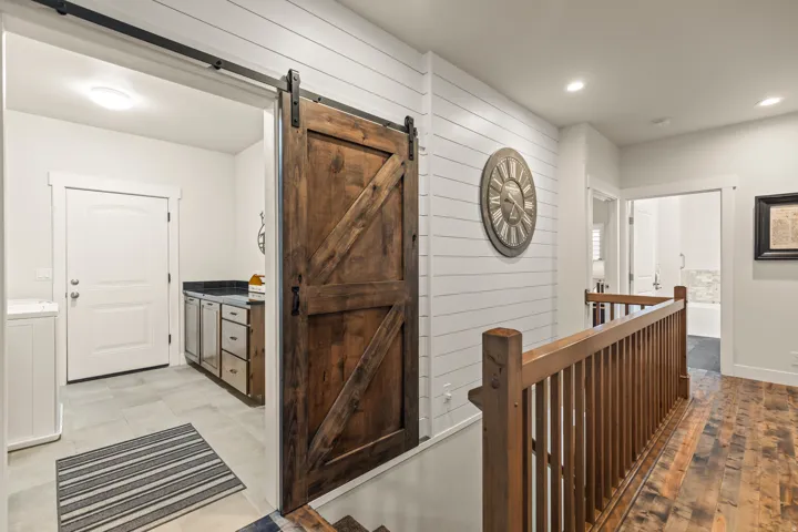 Wood-finish flooring and a wood balustrade frame a hallway with shiplap wall detailing