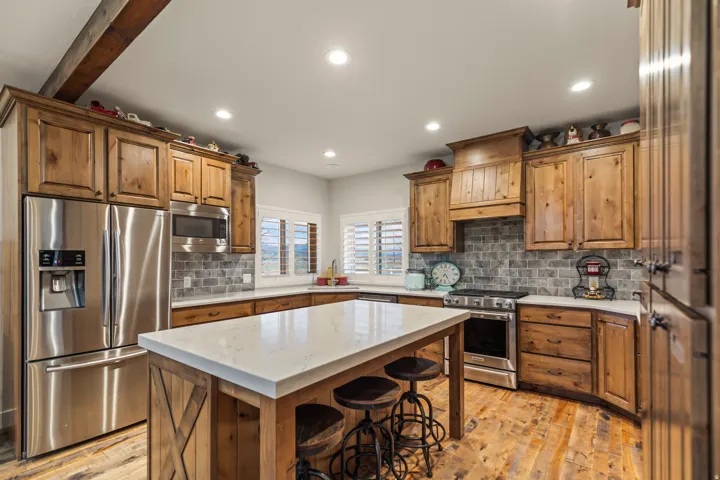 Kitchen featuring wood-finish cabinetry, stainless steel appliances, a white island countertop, and a gray tile backsplash