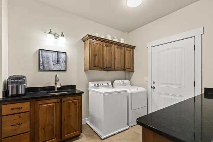 Dedicated laundry area featuring a utility sink with a brushed nickel faucet, dark stone countertops, and wood-finish cabinetry