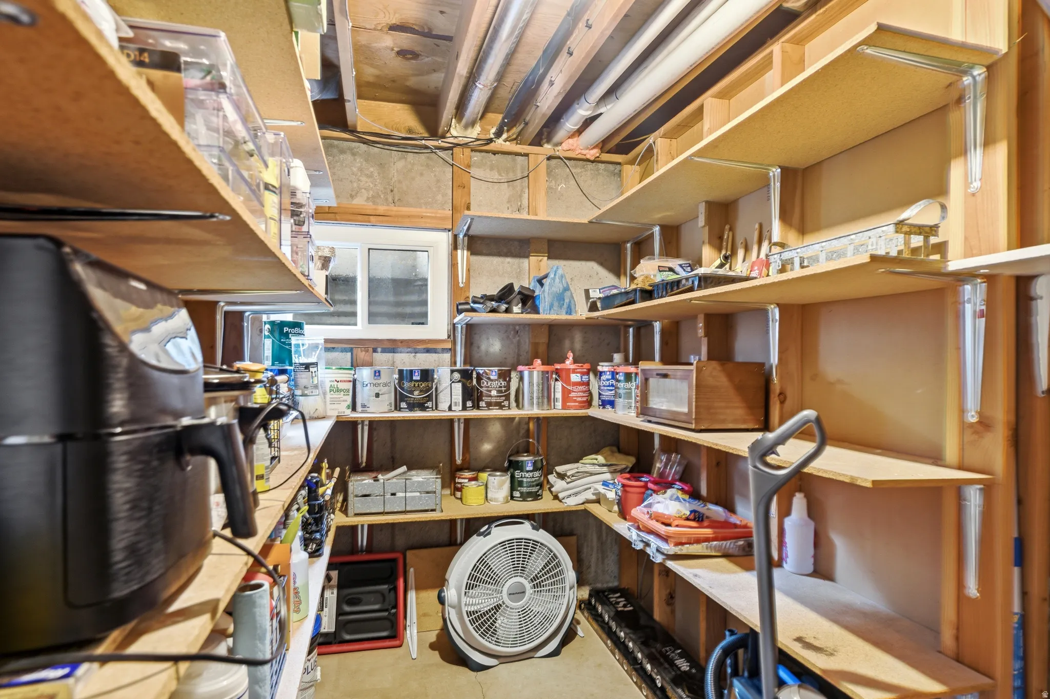 Utility room with extensive built-in wooden shelving, exposed ceiling joists, and a casement window