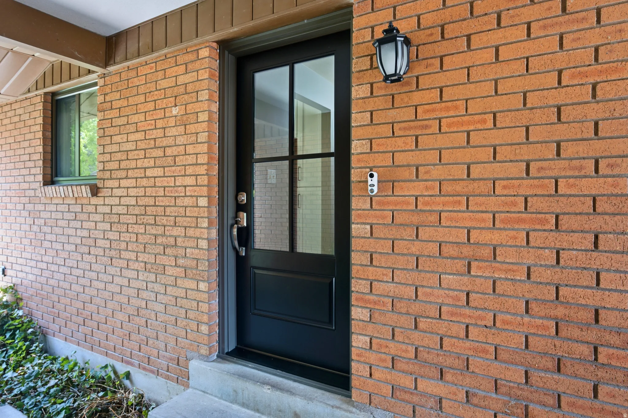 Brick facade featuring a dark-framed entry door with glass panels and an overhead lantern-style light fixture