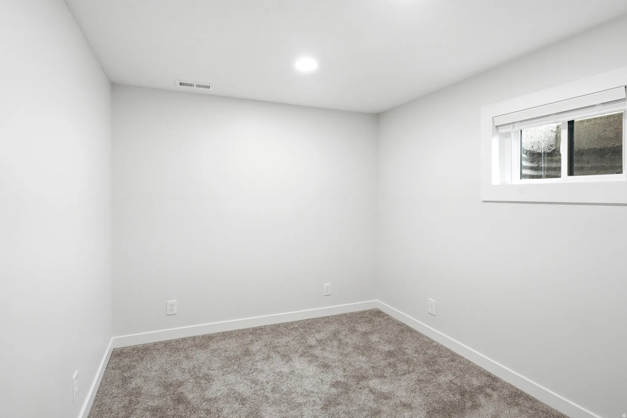 Room with light gray walls, gray carpet flooring, white baseboards, and a white-framed window