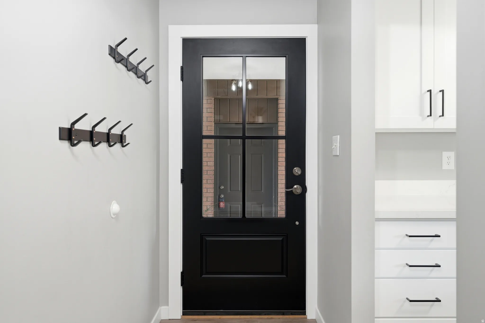 Entryway featuring a black paneled door with glass inserts, bright white trim, light gray walls, built-in white cabinetry, and matte black hardware