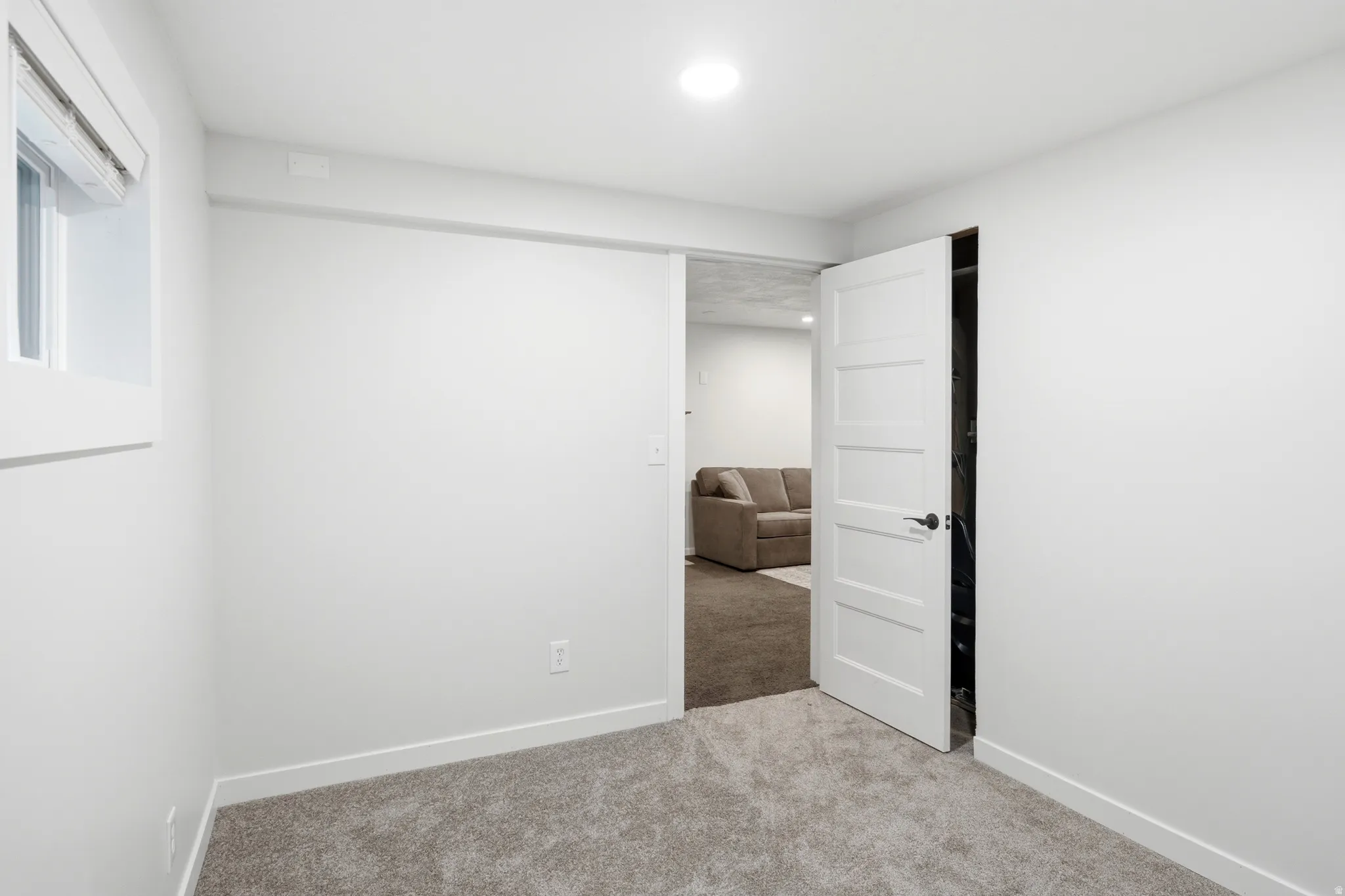 Bright room featuring light gray carpeting, white walls, a recessed ceiling light, and a window with white trim