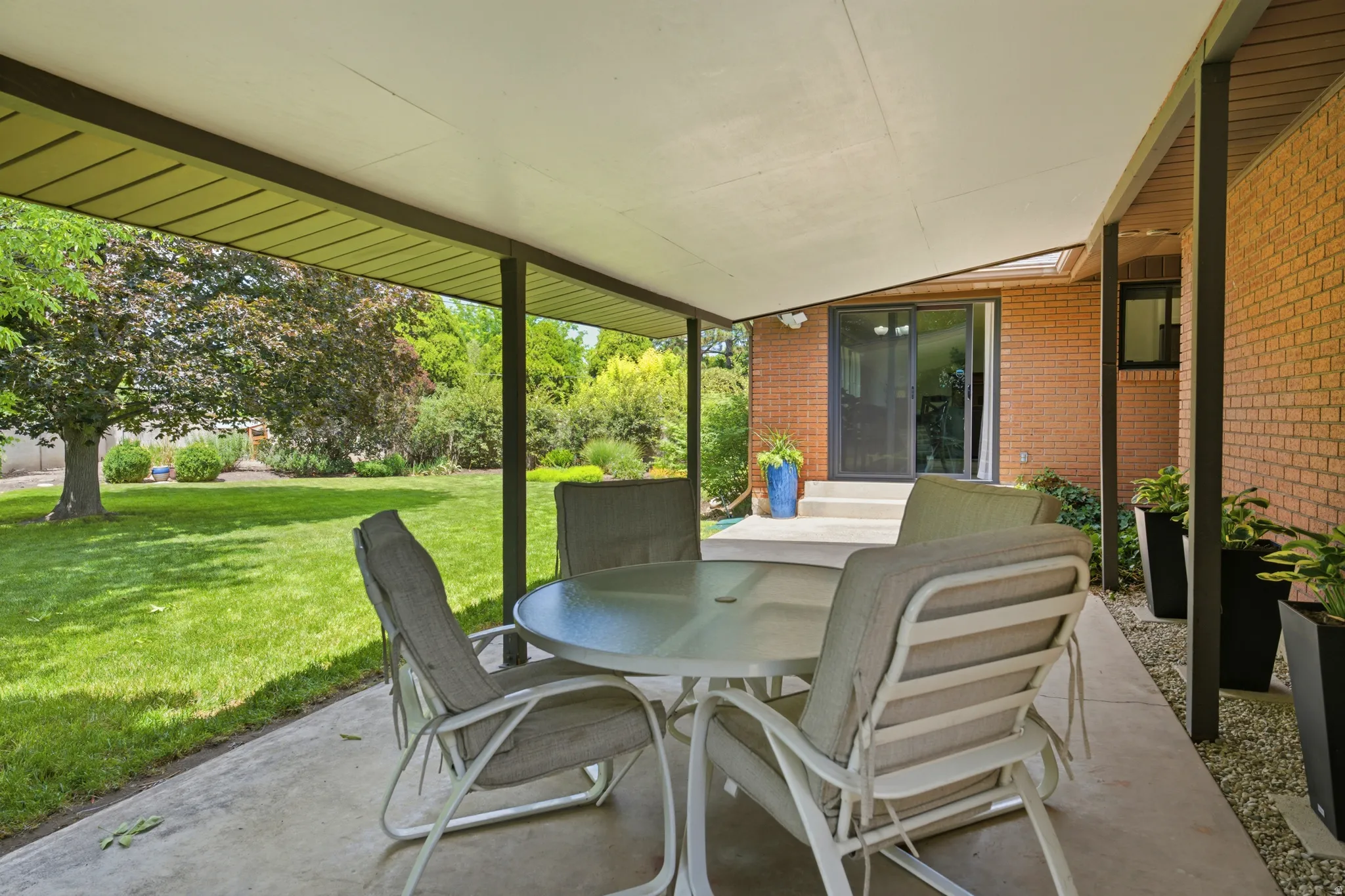 Covered patio space featuring a concrete slab, brick exterior, and direct access to a large green lawn