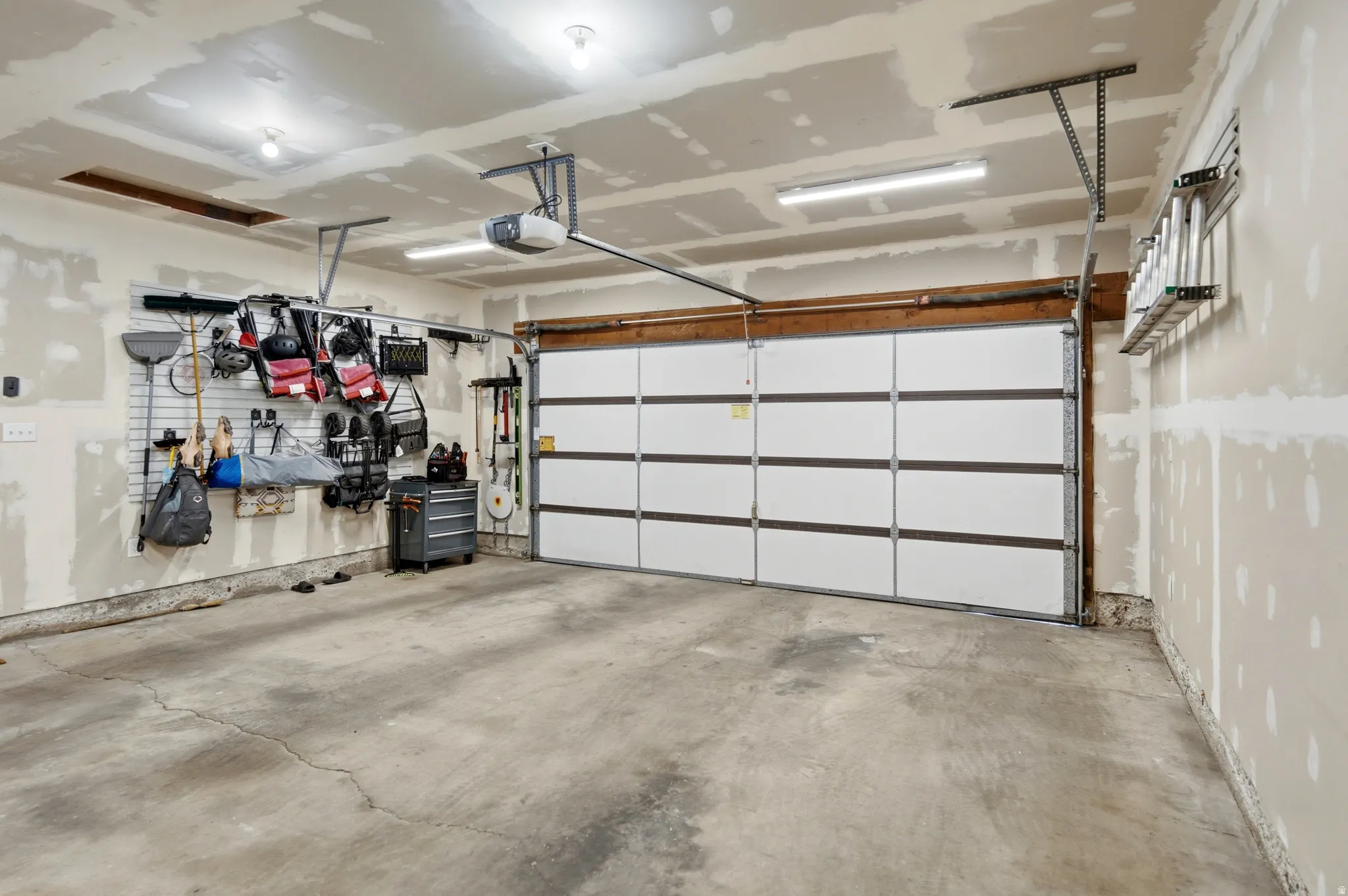 Spacious garage featuring a concrete floor, an overhead door with an automatic opener, exposed drywall, and built-in wall organization systems
