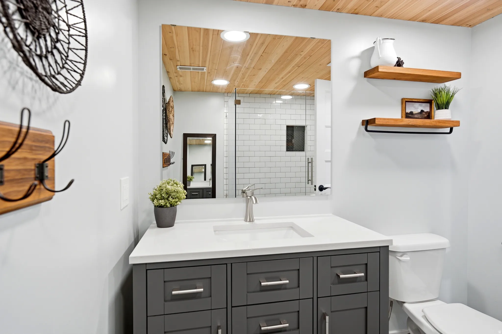 Bathroom featuring a wood-finish plank ceiling, a vanity with a white countertop and dark gray cabinetry, a rectangular undermount sink, and a mirrored medicine cabinet