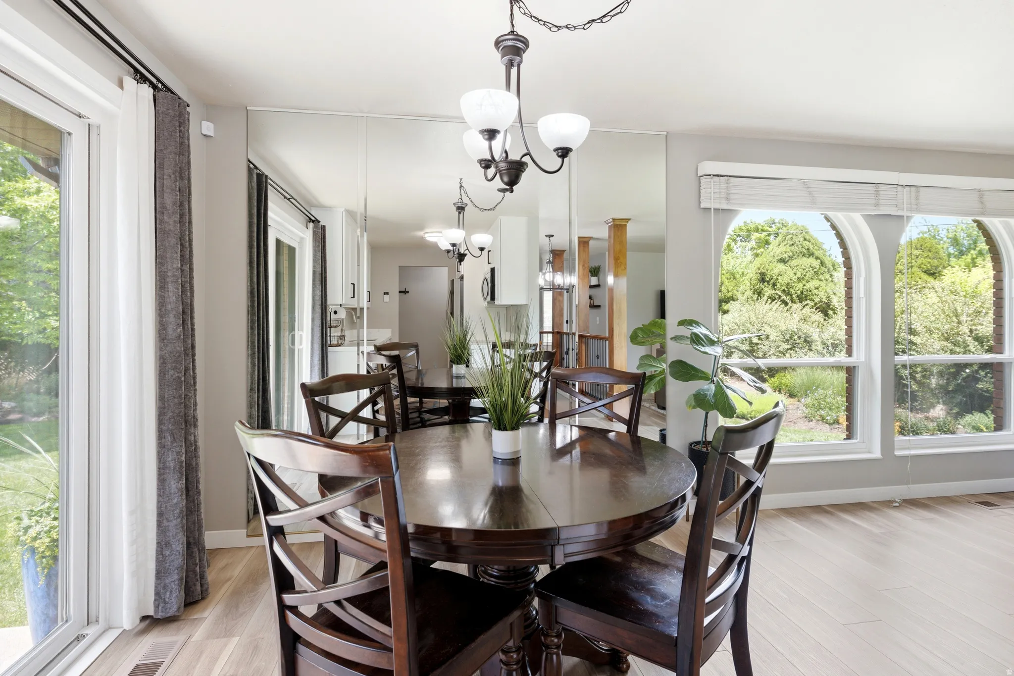Dining area featuring wood-finish flooring, a contemporary chandelier, mirrored accent wall, and arched windows