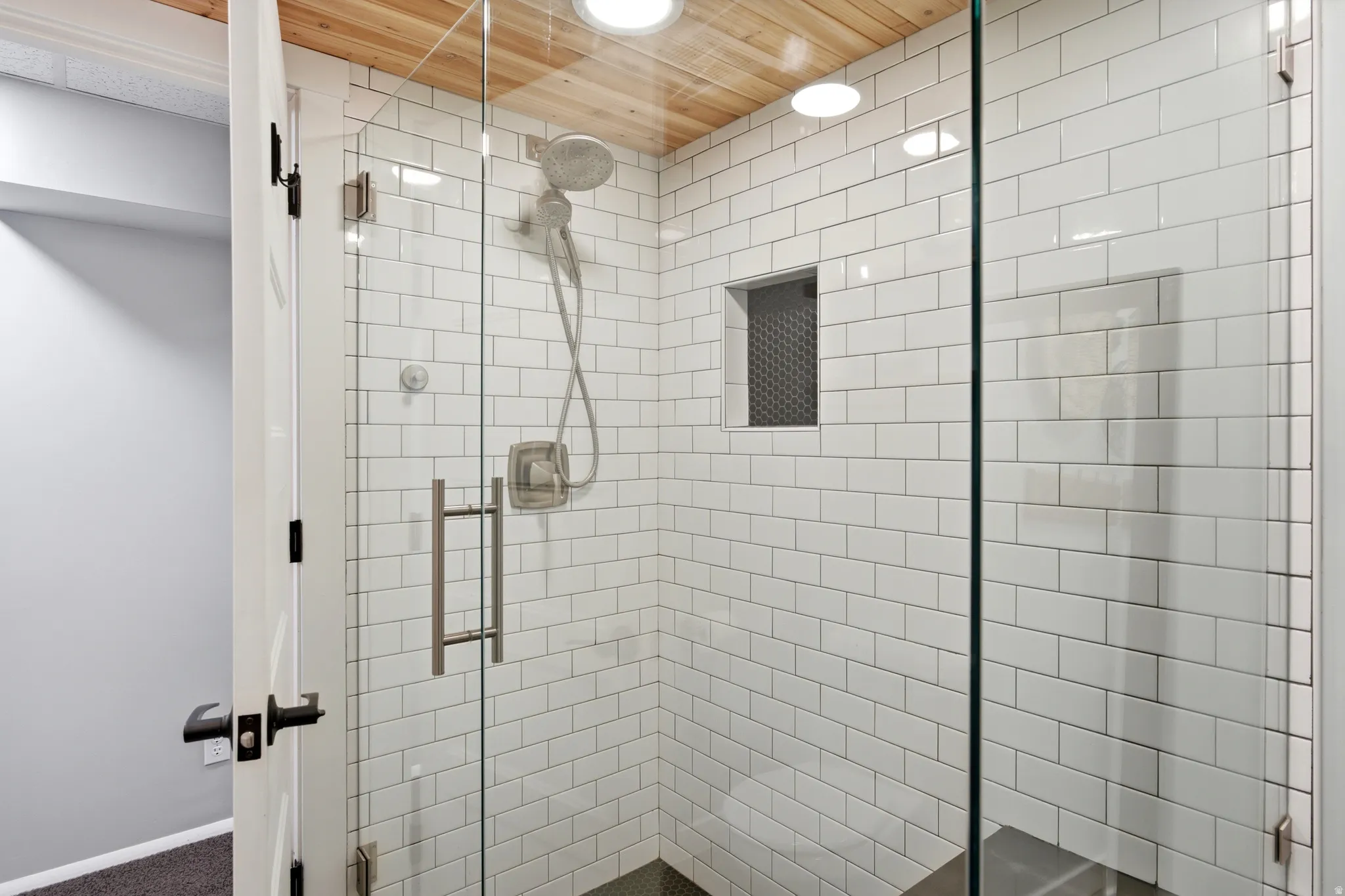 Glass-enclosed shower featuring white subway tile, a built-in shower niche with mosaic tile, and a wood-finish ceiling with recessed lighting