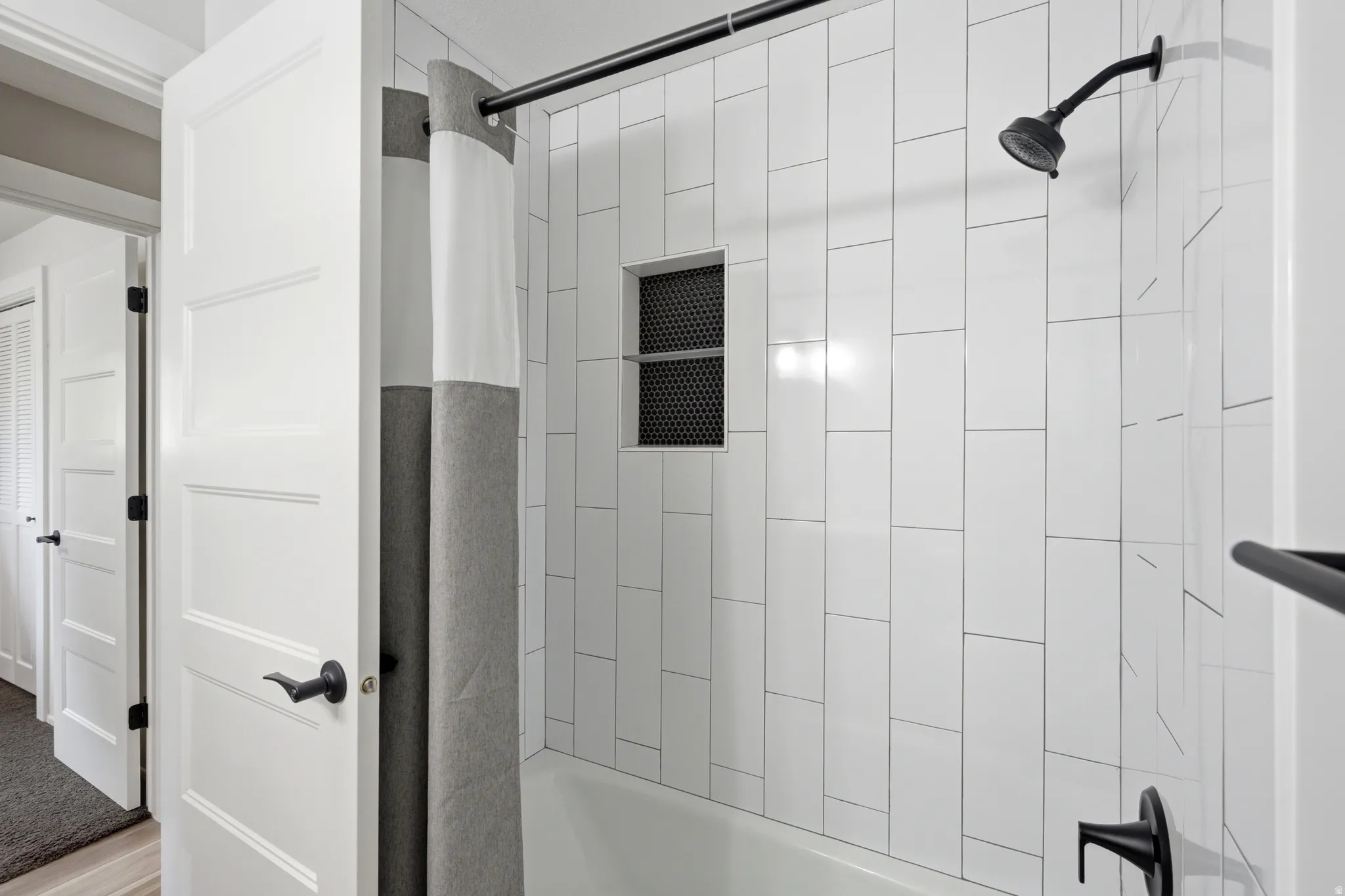 Bathtub with white subway tile surround, recessed shower niche with dark perforated metal accent, and matte black shower fixtures