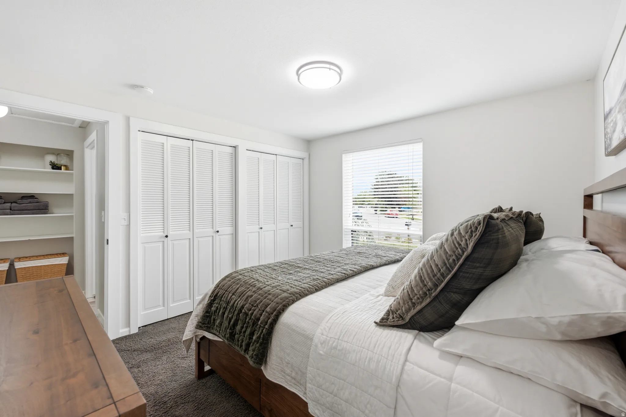 Bedroom featuring light grey wall paint, dark grey carpet flooring, a flush-mount ceiling light fixture, a window with horizontal blinds, and louvered bi-fold closet doors