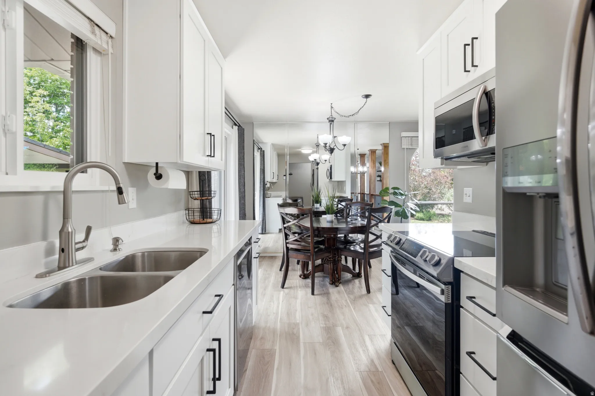 Bright kitchen featuring white cabinetry, light countertops, stainless steel appliances, and wood-finish flooring