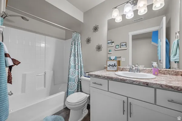 Bathroom featuring a white tub/shower combination with a chrome showerhead, a vanity with a white oval sink, a speckled countertop, white cabinetry with silver hardware, and a large wall-mounted mirror with a multi-bulb light fixture