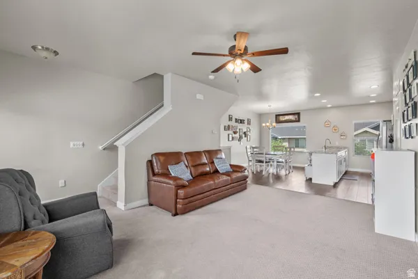 Open-concept living area featuring a ceiling fan, recessed lighting, neutral wall tones, and contrasting wood-finish flooring in the dining and kitchen areas