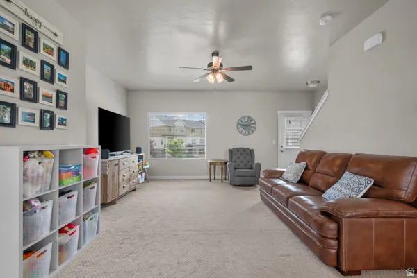 Light-filled living area featuring neutral carpet flooring, recessed lighting, and a ceiling fan