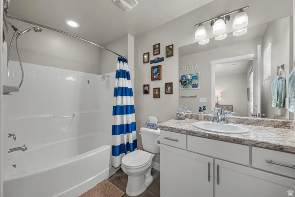 Full bathroom featuring a white tub with an integrated shower, a white toilet, and a vanity with a white countertop and undermount sink