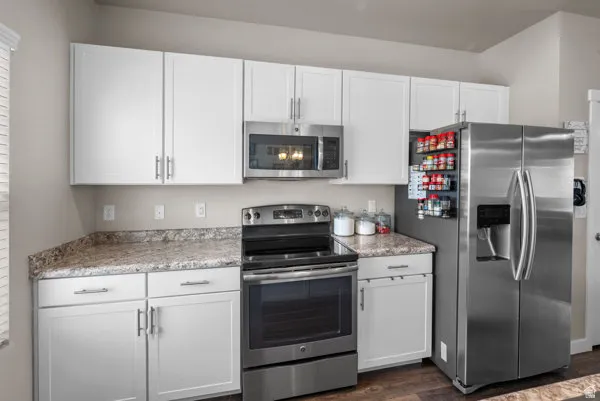 Modern kitchen featuring white cabinetry, stone-look countertops, stainless steel appliances, and wood-finish flooring