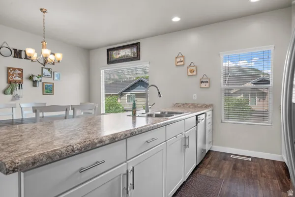 Kitchen featuring a double basin sink with a gooseneck faucet, light-toned countertops, white cabinetry with brushed nickel hardware, and wood-finish flooring