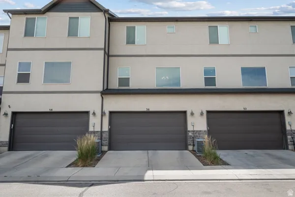 Contemporary townhome exterior featuring a stucco finish, multiple windows, and individual garage doors