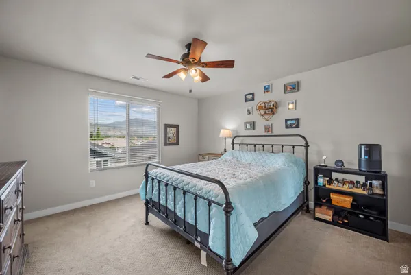 Bedroom featuring a ceiling fan with integrated lighting, a large window offering mountain scenery, neutral wall paint, and carpet flooring