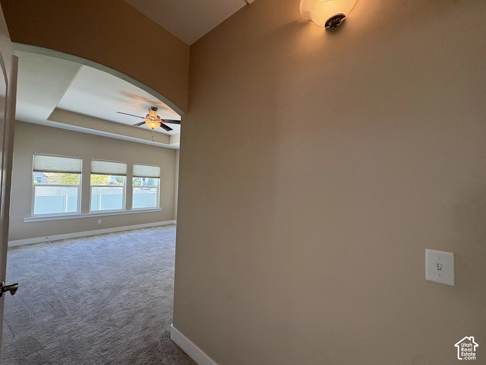 Recessed ceiling featuring a ceiling fan, arched doorway, and triple windows