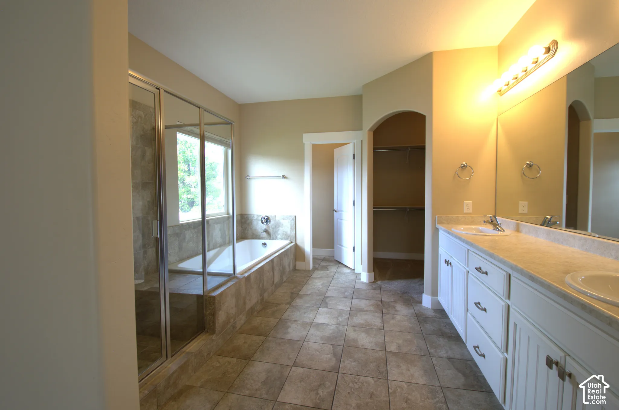 Spacious master bathroom featuring a dual vanity, tiled flooring, built-in soaking tub, and a glass-enclosed shower with tile surround