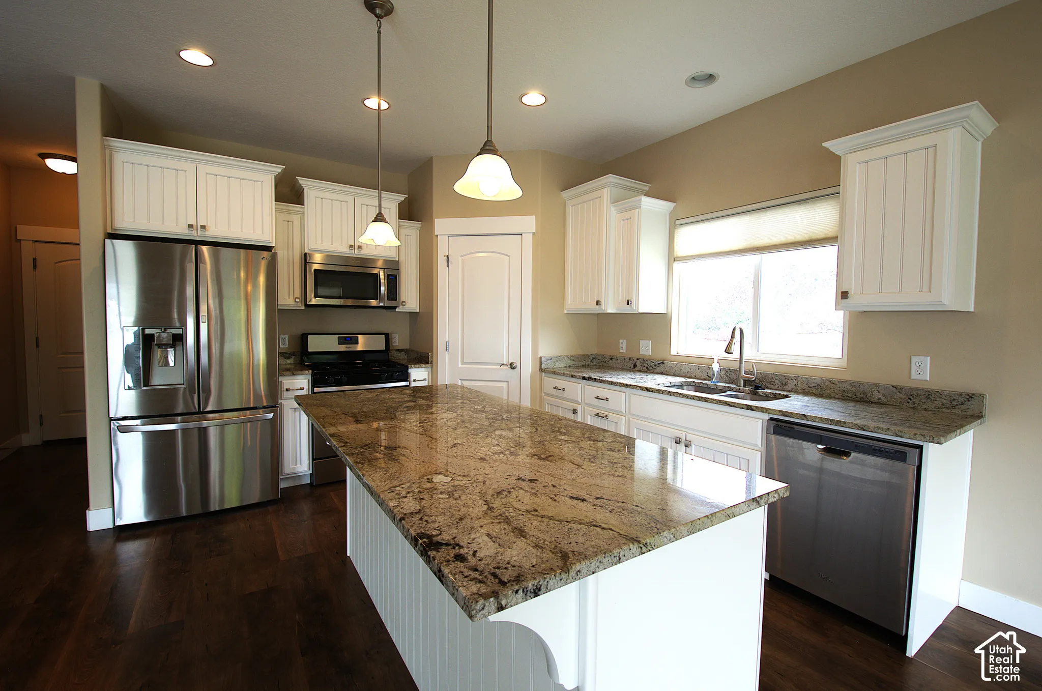 Spacious kitchen featuring a large island with a stone countertop, white cabinetry, and stainless steel appliances including a refrigerator, microwave, range, and dishwasher