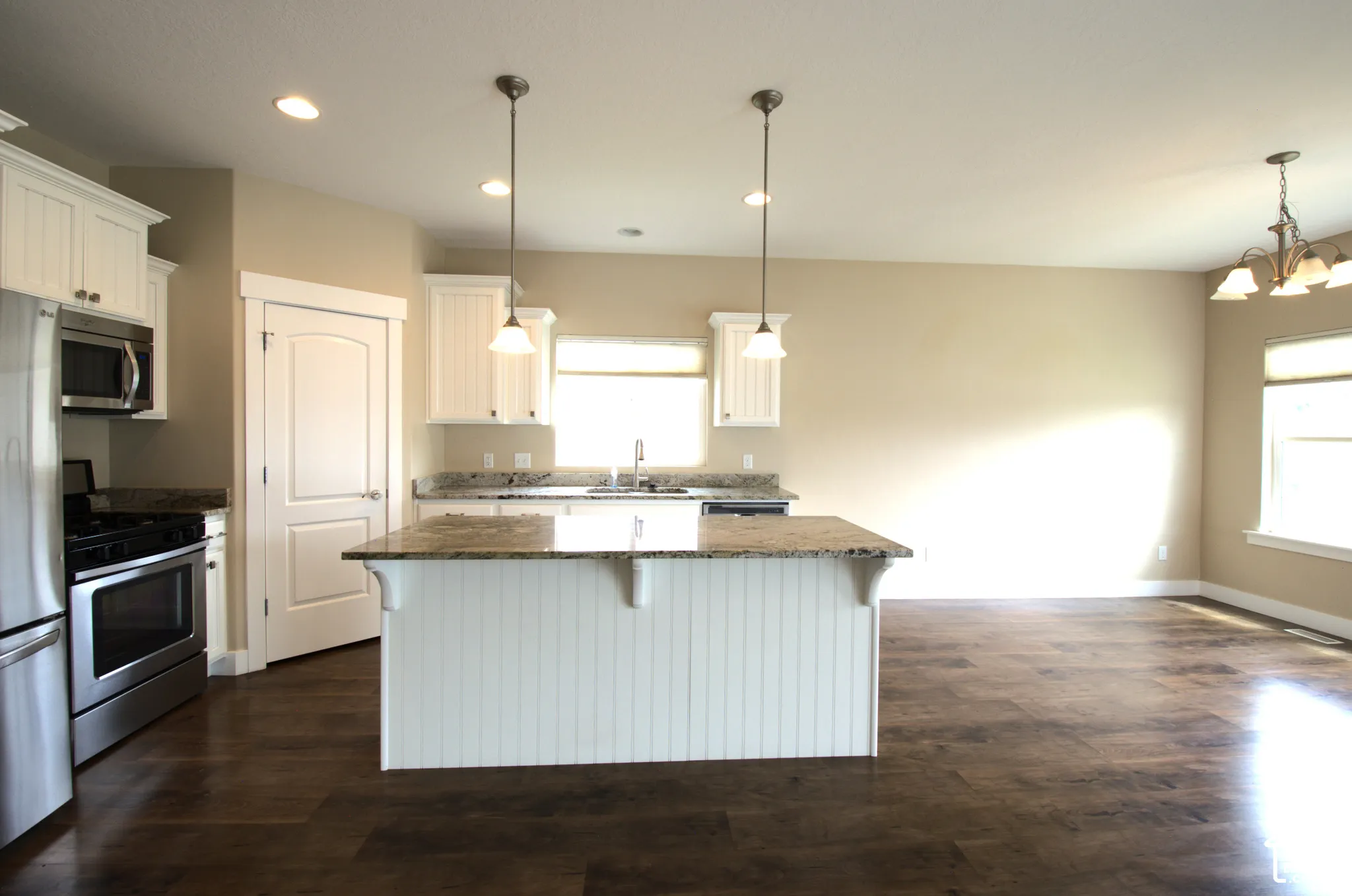 Kitchen featuring an island with beadboard paneling, pendant lighting, white cabinetry, granite countertops, and stainless steel appliances