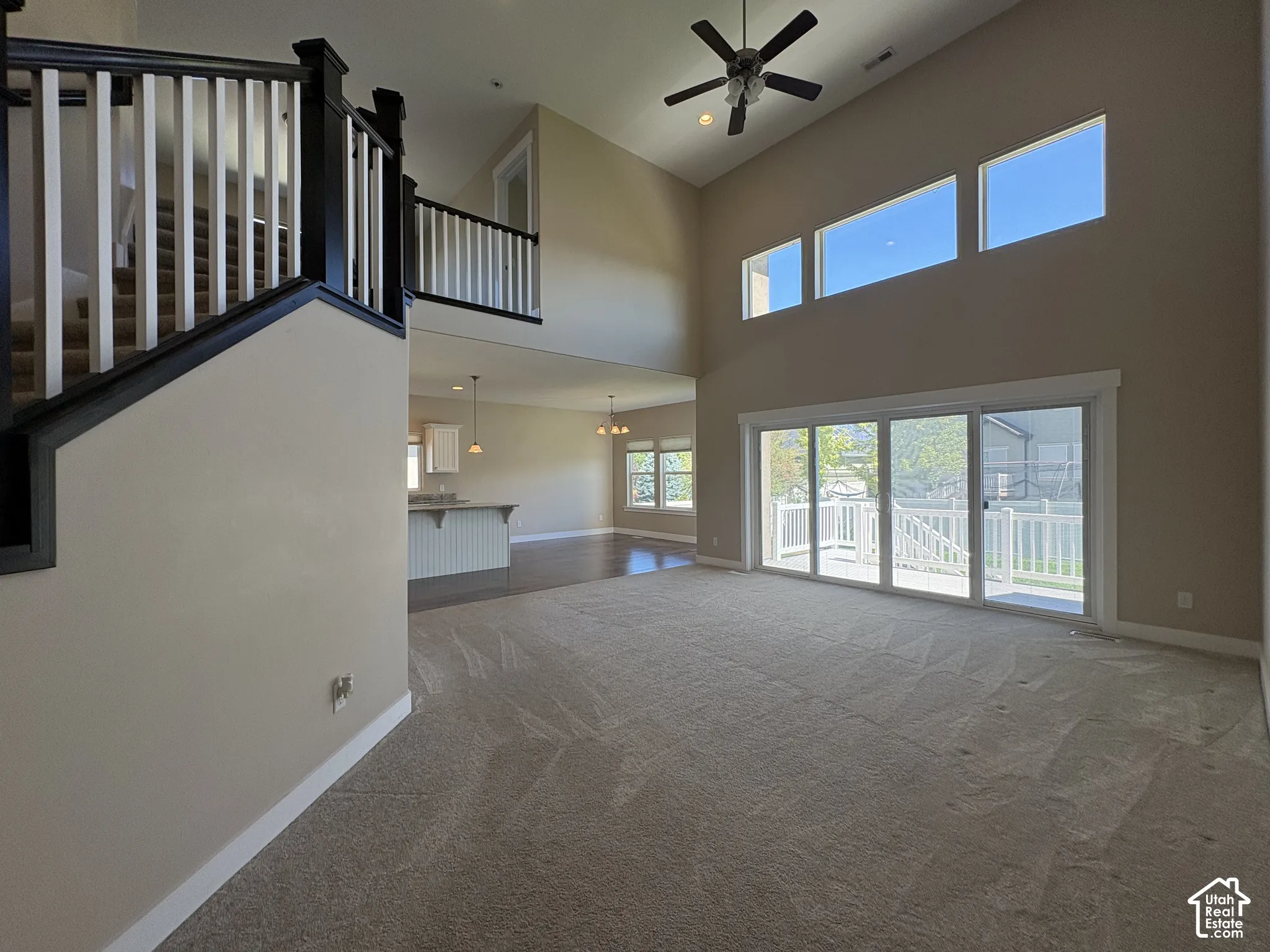 Open-concept living area with soaring ceilings, ceiling fan, and abundant natural light from expansive glass sliding doors and transom windows