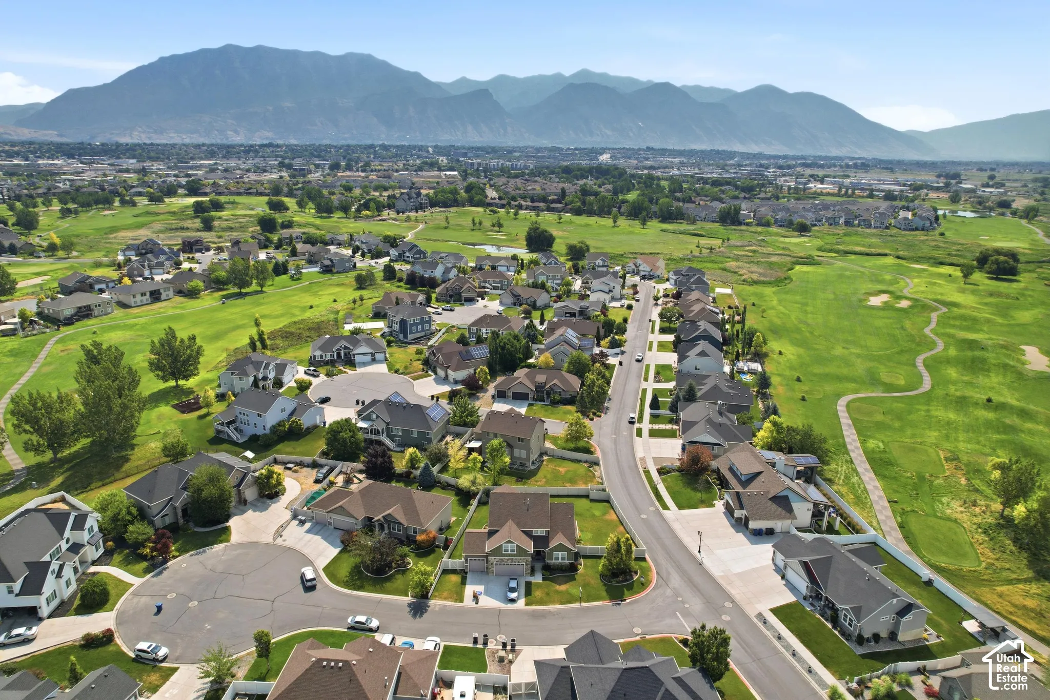 Expansive neighborhood featuring residential properties bordering green spaces and golf course fairways, with a mountain range backdrop