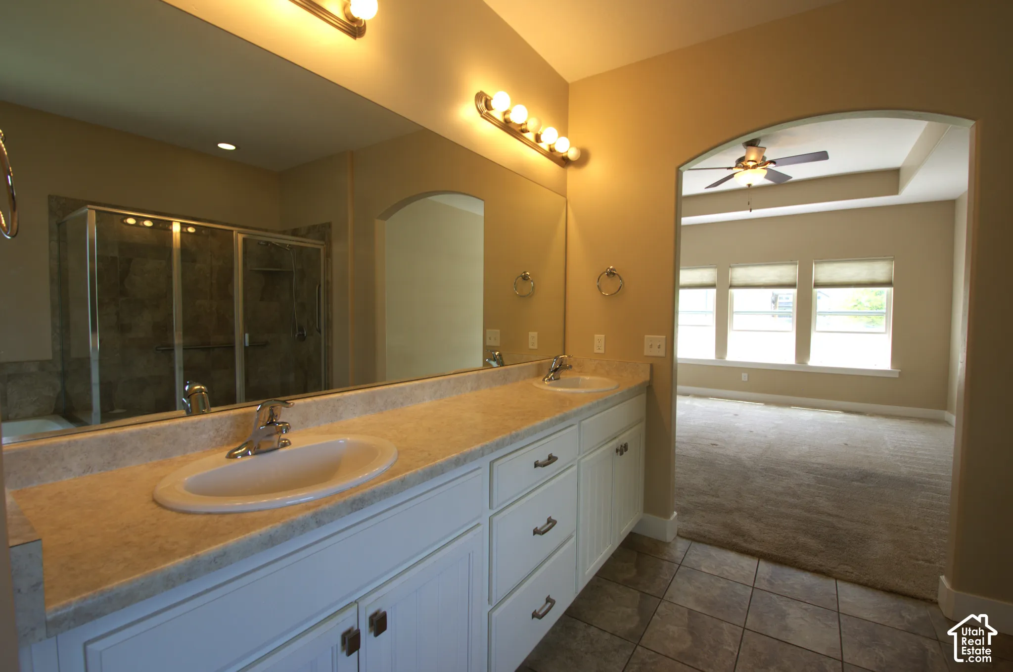 Master Bathroom featuring a dual vanity with a light-toned countertop, a large wall-mounted mirror, and a glass-enclosed shower