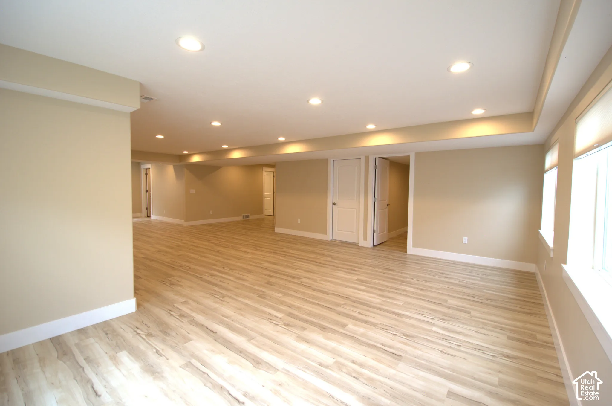 Expansive room featuring light wood-finish flooring, recessed lighting, neutral wall tones, multiple windows with blinds, and white trim throughout