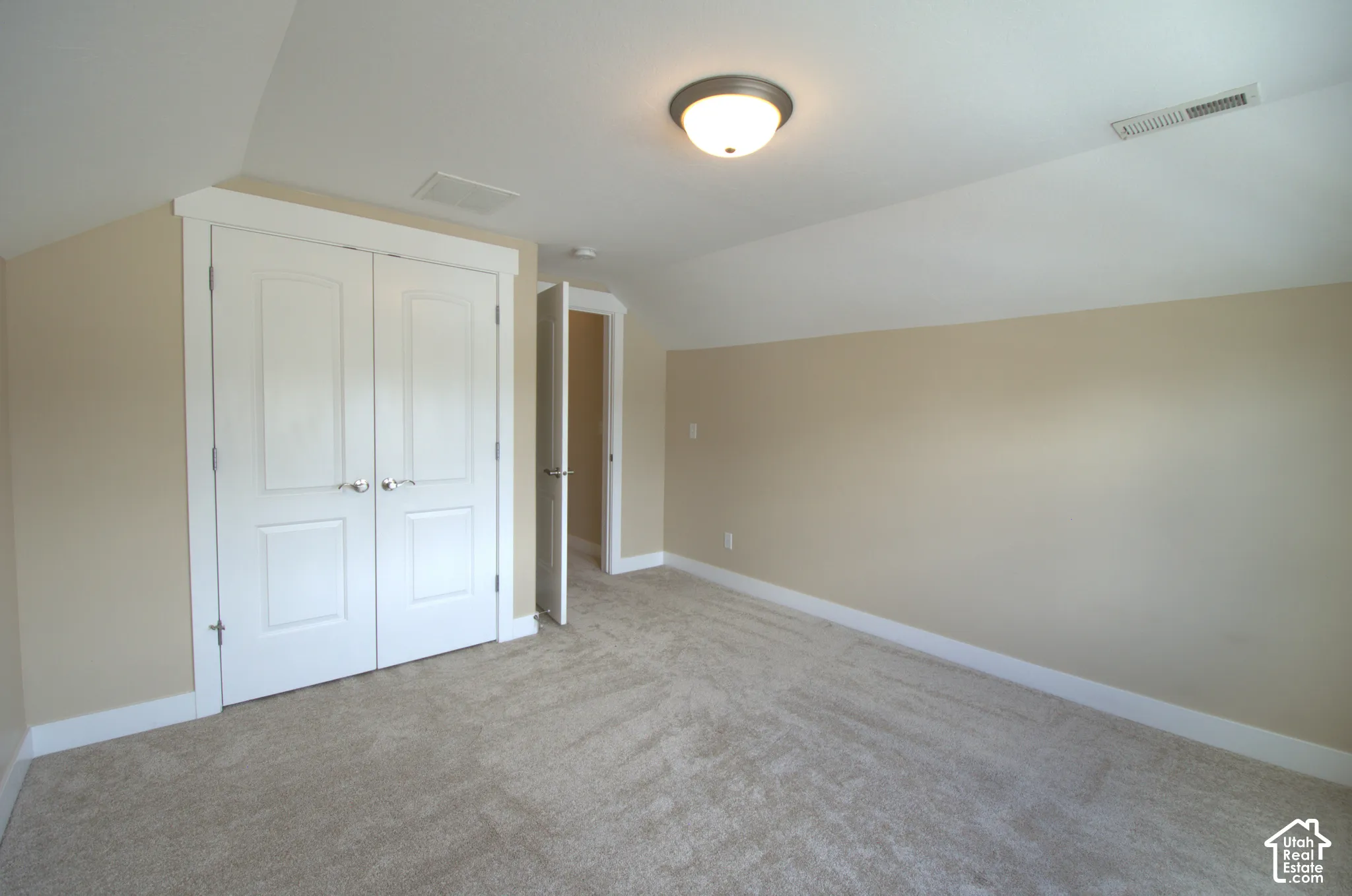 Carpeted room with a vaulted ceiling, painted walls, white trim, and a double-door closet