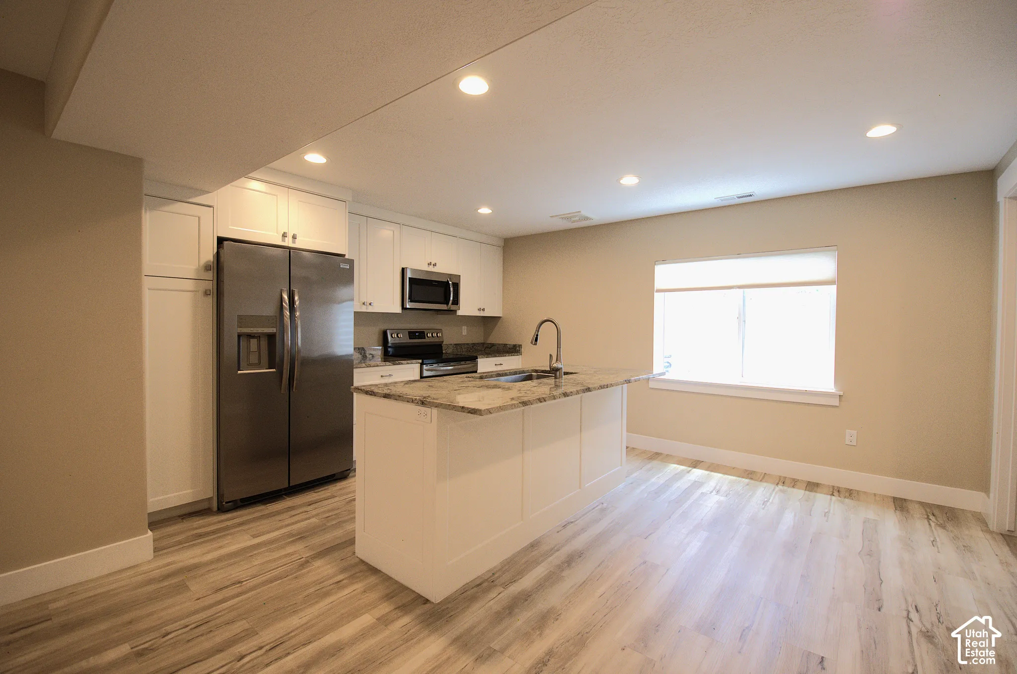 Kitchen featuring a center island, stainless steel appliances, white cabinetry, and wood-finish flooring