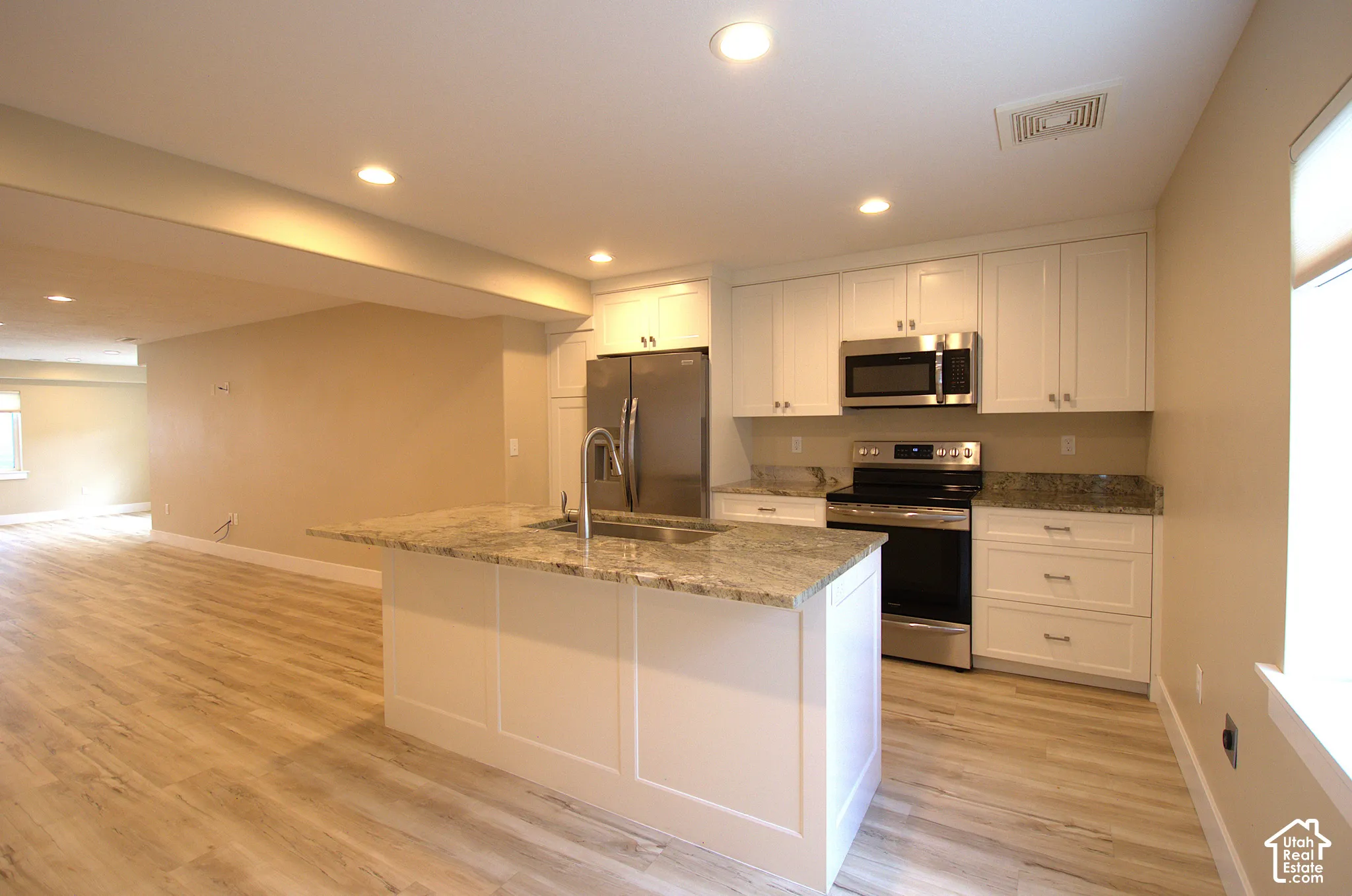 ADU Kitchen featuring an island with a built-in sink, white shaker-style cabinetry, stainless steel appliances, recessed lighting, and wood-finish flooring