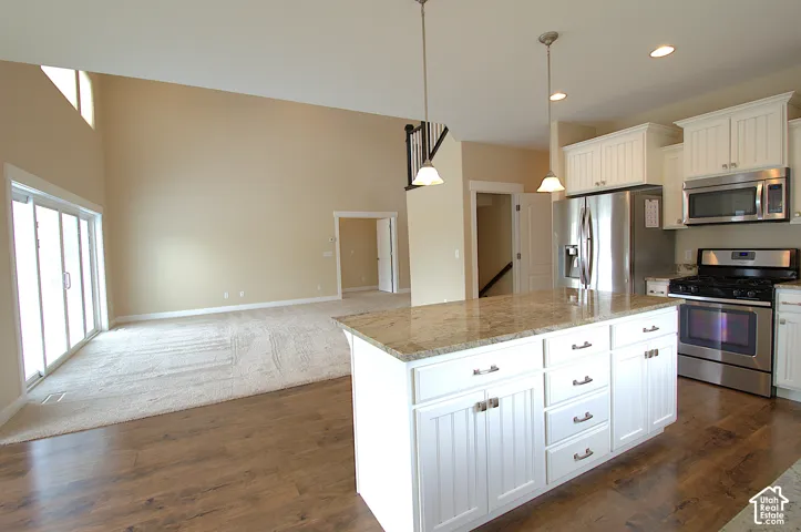Open-concept kitchen featuring white cabinetry, stainless steel appliances, and a central island with a stone countertop