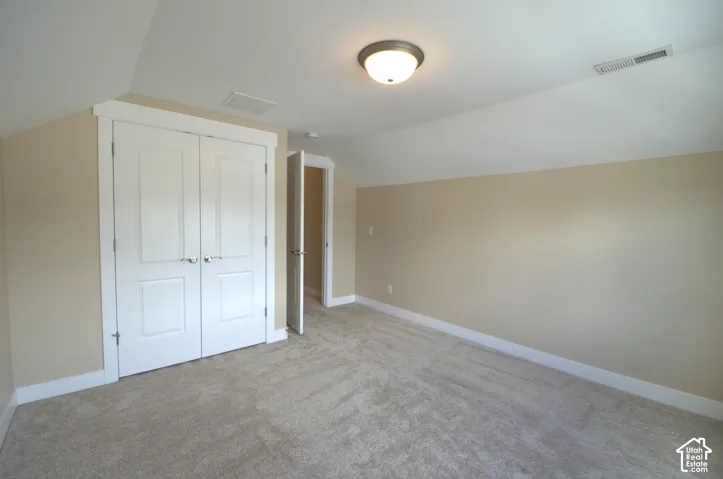Carpeted room with a vaulted ceiling, painted walls, white trim, and a double-door closet