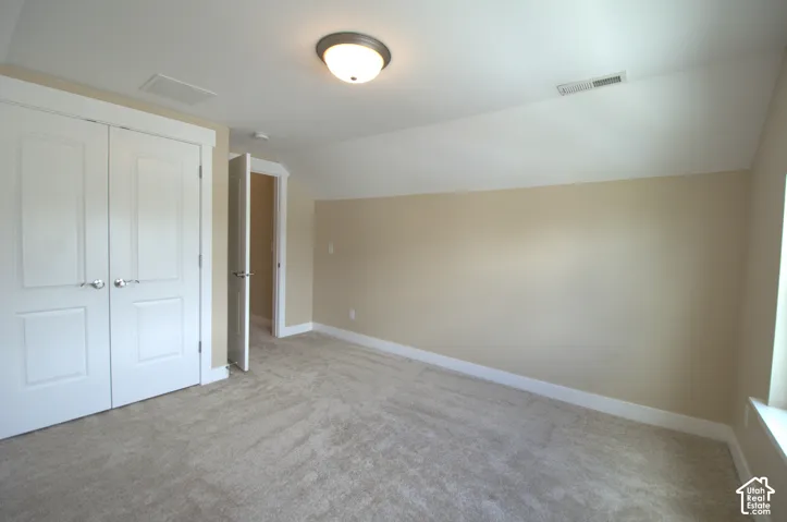 Spacious room featuring neutral carpeting, a double-door closet, and a flush-mount ceiling light fixture